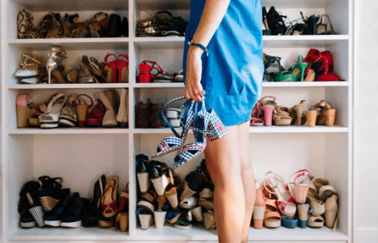 femme tenant des chaussures devant un placard rempli de chaussures