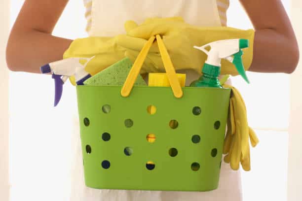 Gros plan sur un panier vert avec produits ménagers que tient une femme aux mains gantées