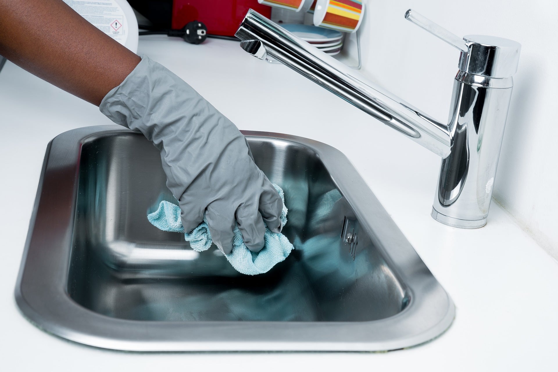 Un main avec gant de vaisselle qui nettoie un évier